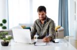 Man sitting at the laptop and smiling while writing down information